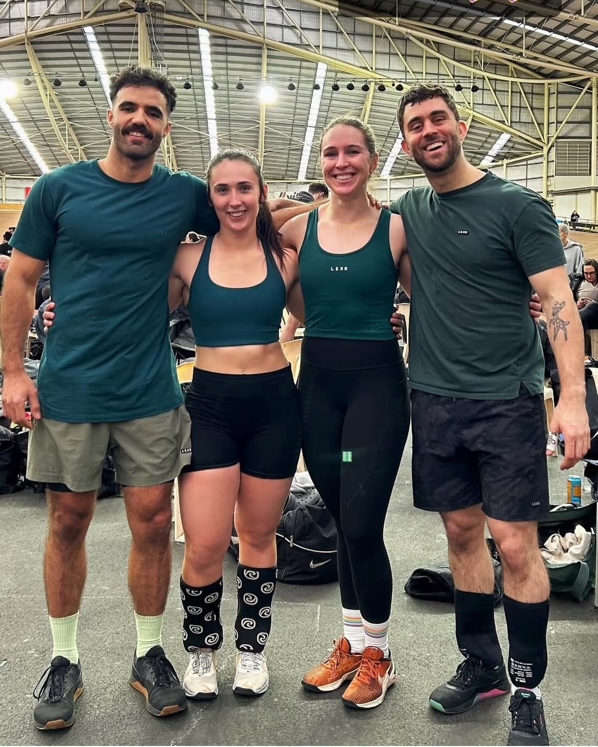 Emily and 3 other people smiling with their arms linked around each other. They are wearing matching coloured sports wear.