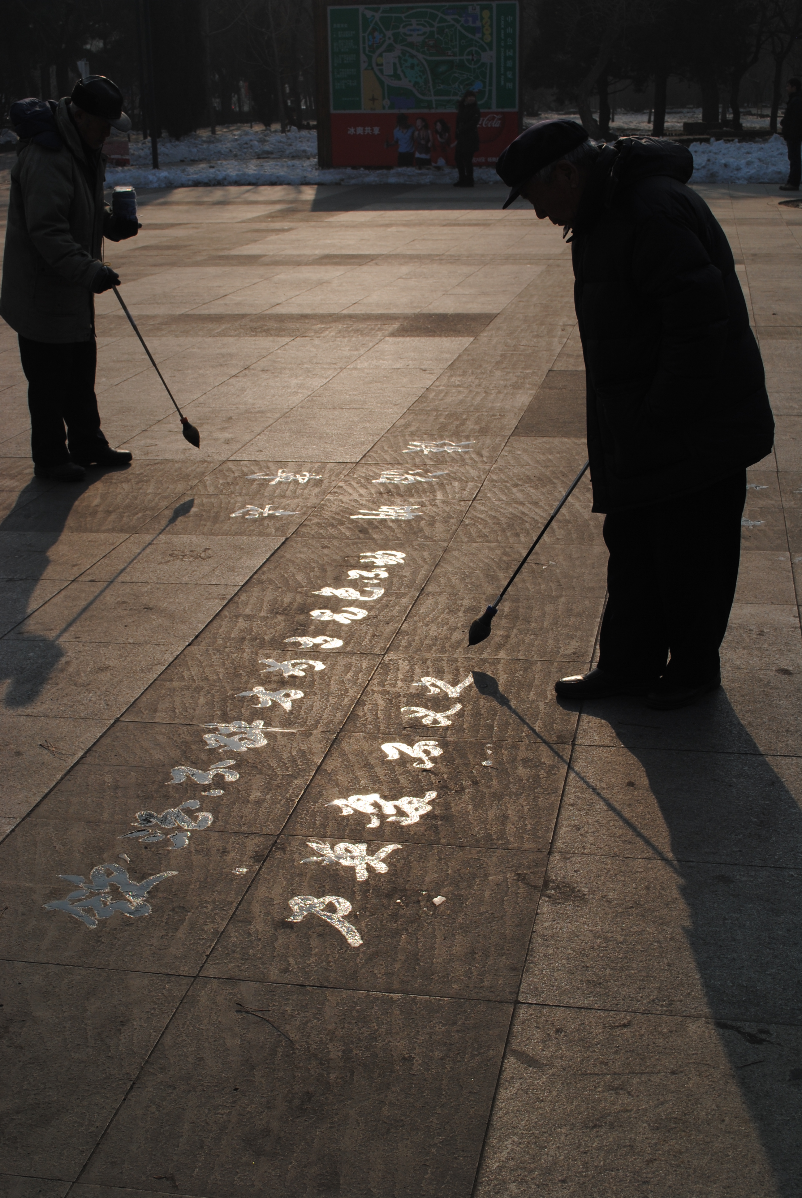 Two Chinese men are writing calligraphy on the concrete in an outdoor area