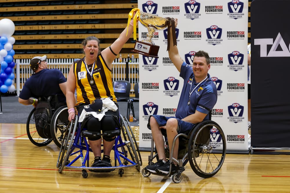 Two people in wheelchairs are side by side holding up the VWFL cup