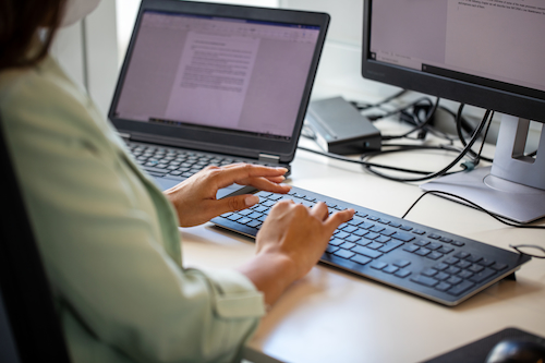 A woman is shown from behind typing and looking at a computer screen. 