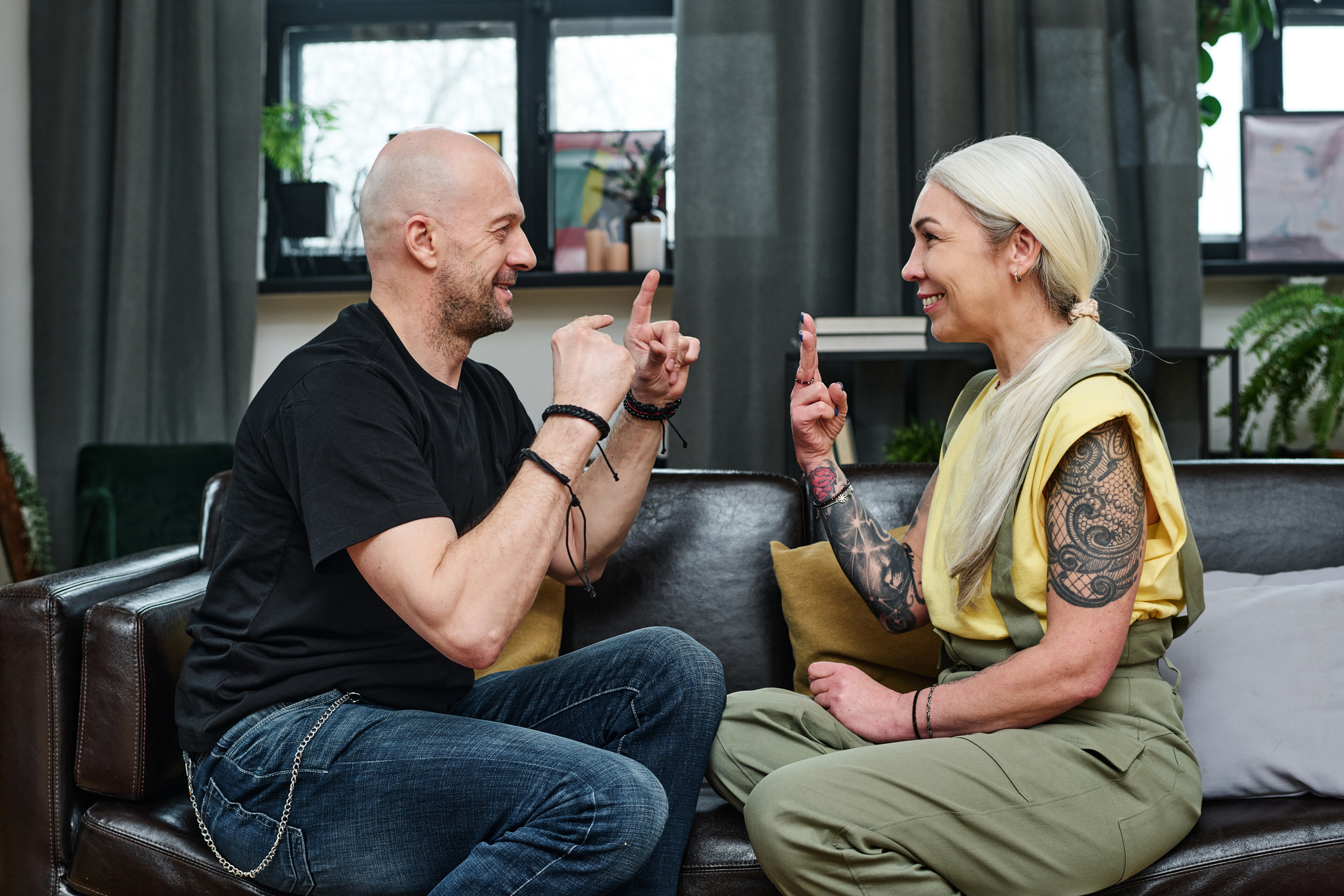 A man and woman are sitting on a couch facing each other. They are communicating using sign language.