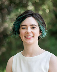 A head and shoulders photo of Annie. They are wearing a white top and have short dark hair with blue highlights.